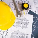 Engineer workplace with blueprints, protractor and safety helmet.